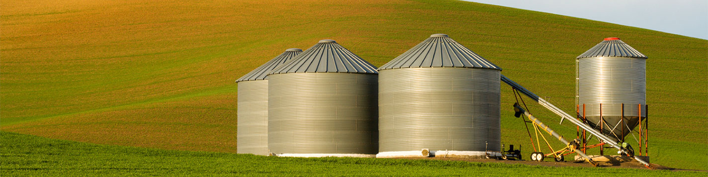 A grain bin and agriculture equipment set against a green field.